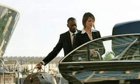 A man and woman in suits are loading bags into the car.