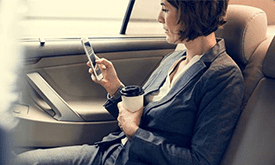 A woman sitting in the back of a car holding her phone.